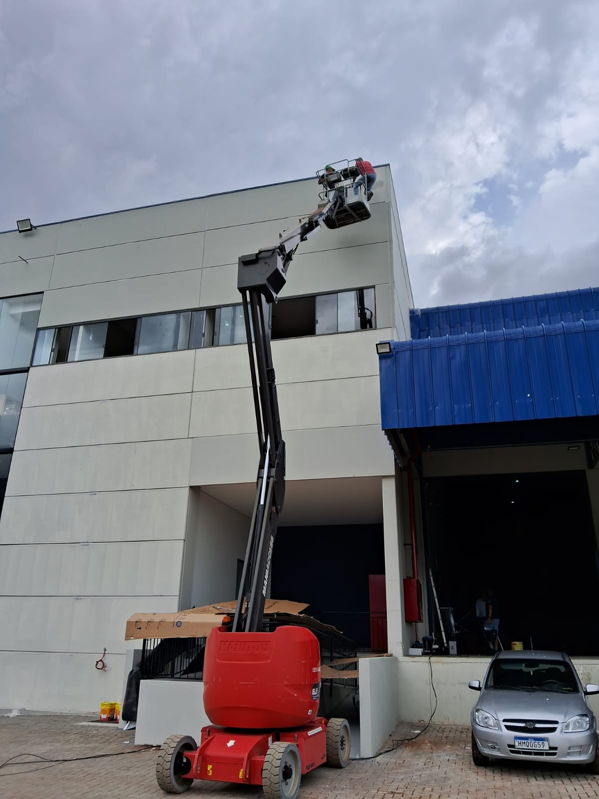 Fachada de galpão industrial sendo pintada com plataforma elevatória