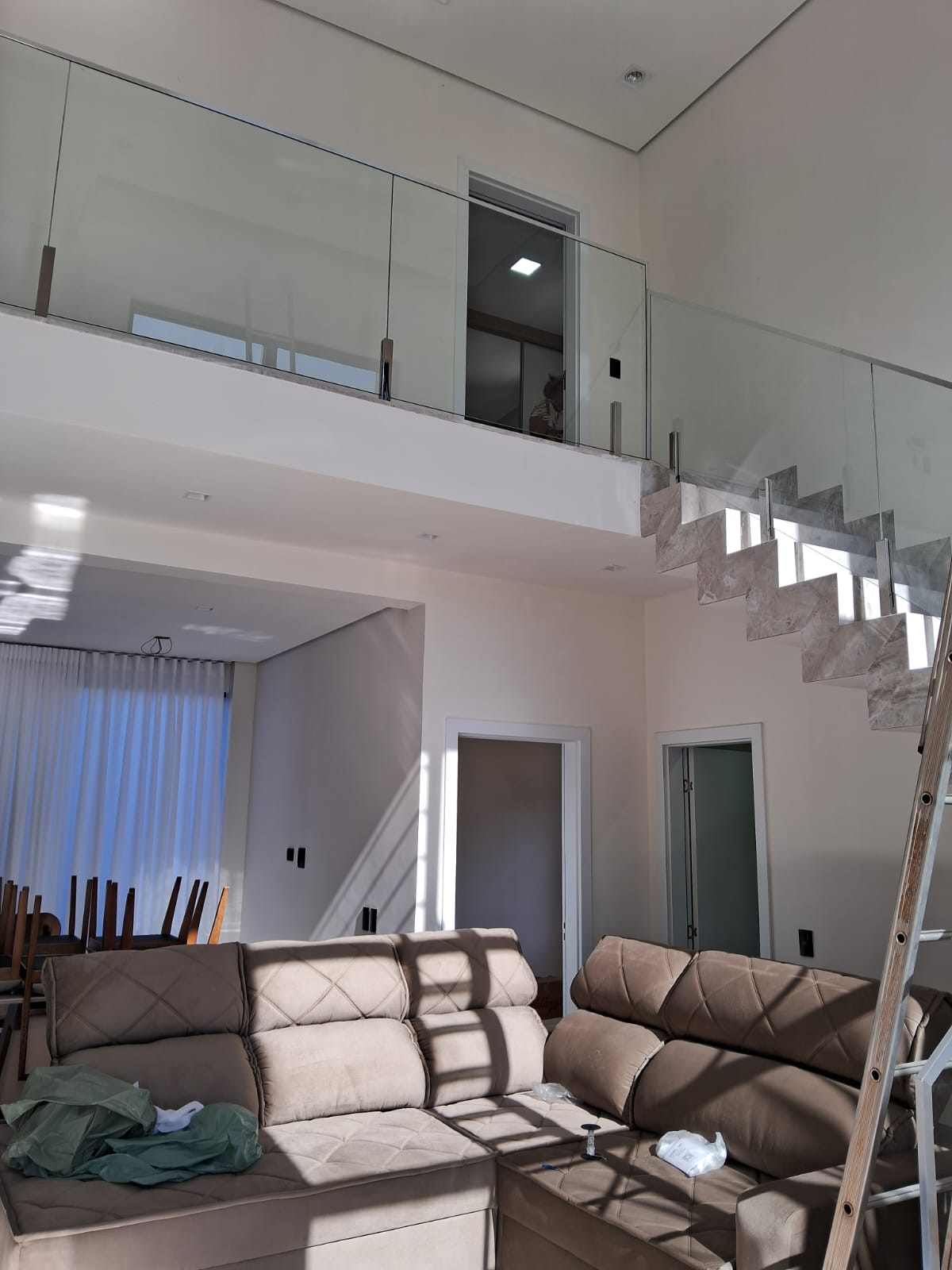 Sala de estar ampla com paredes claras pintadas e escada com guarda-corpo de vidro